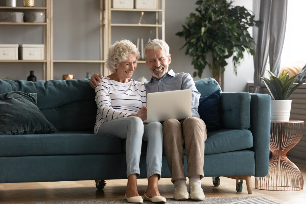 Senior couple sitting on sofa smiling and looking at laptop together